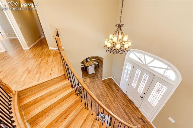 19340 Furrow Road Monument, CO 80132 - Photo 24 of 50 Entrance foyer with stairs, an inviting chandelier, a high ceiling, arched walkways, and wood finished floors