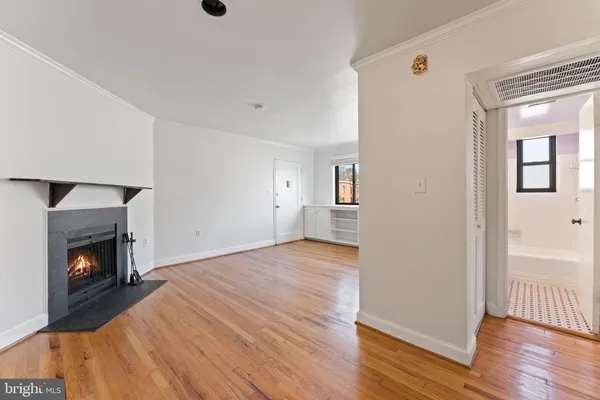 a view of an empty room with wooden floor fireplace and a window