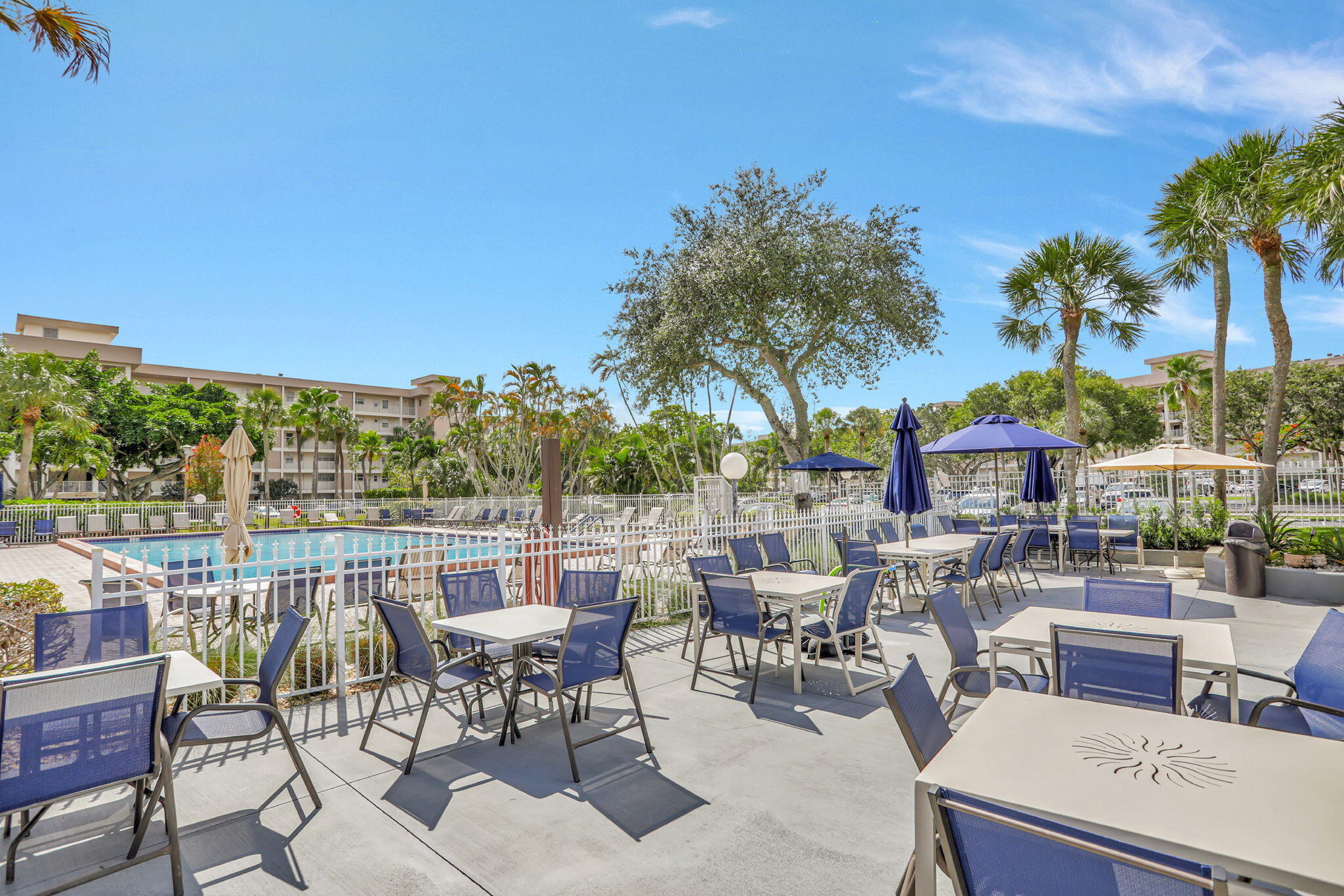 3100 North Palm Aire Drive, Unit 106 Pompano Beach, FL 33069 - Photo 28 of 42 a view of a patio with a table and chairs under an umbrella with palm trees