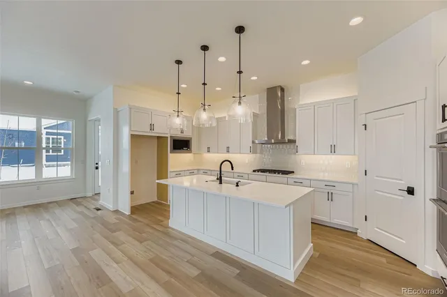 a large kitchen with kitchen island a stove a sink a refrigerator and white cabinets with wooden floor