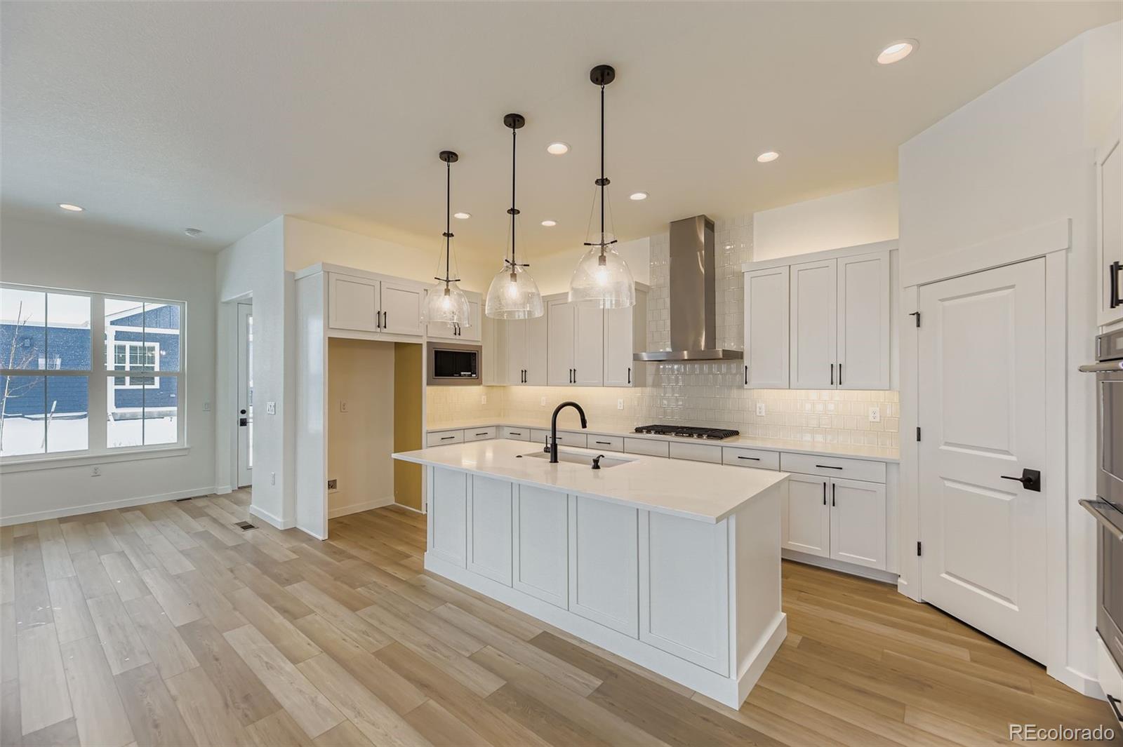 8902 South Riviera Way Aurora, CO 80016 - Photo 8 of 26 a large kitchen with kitchen island a stove a sink a refrigerator and white cabinets with wooden floor