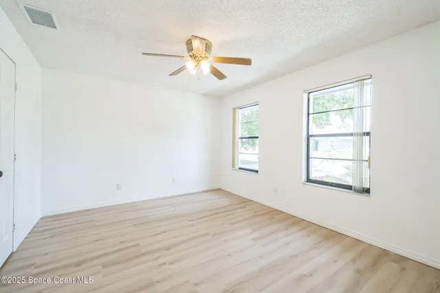 an empty room with wooden floor fan and windows