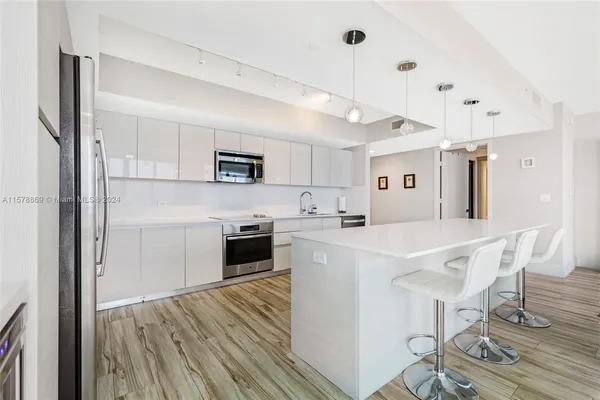 a kitchen with stainless steel appliances a stove a sink dishwasher a refrigerator white cabinets and wooden floor next to a window