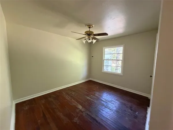 an empty room with wooden floor chandelier fan and windows