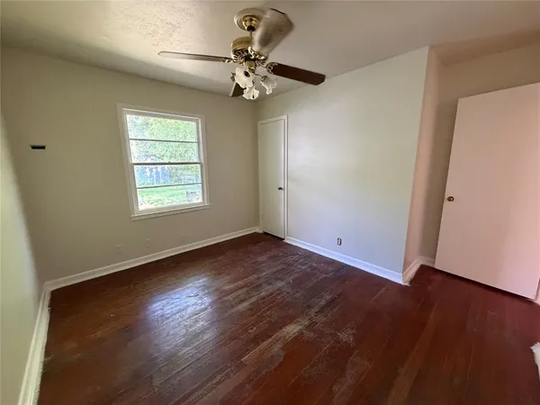an empty room with wooden floor fan and windows