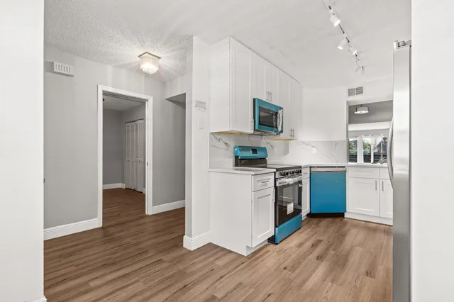 a kitchen with stainless steel appliances granite countertop a refrigerator a sink and white cabinets with wooden floor