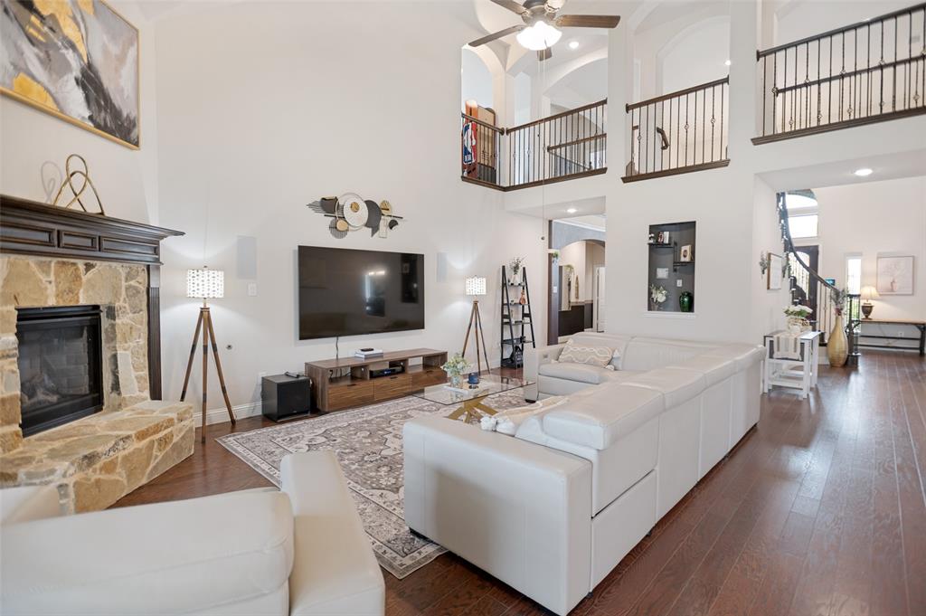 413 Frontier Court Midlothian, TX 76065 - Photo 6 of 26 Two-story living area with high ceilings, featuring a stone-clad fireplace with a dark wood mantel, wood-finish flooring, and a second-story balcony with metal railings