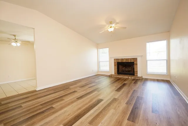 an empty room with wooden floor fireplace and windows