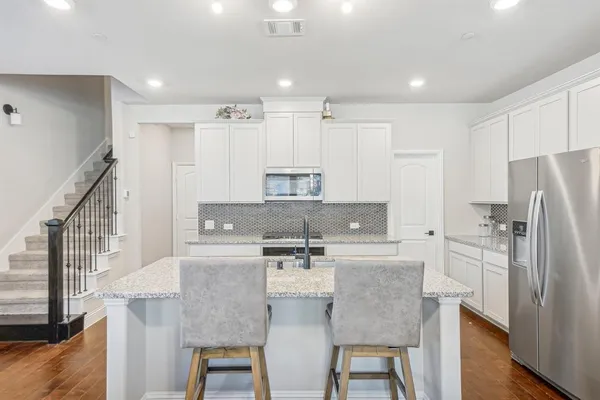 a kitchen with stainless steel appliances granite countertop a dining table chairs refrigerator and sink