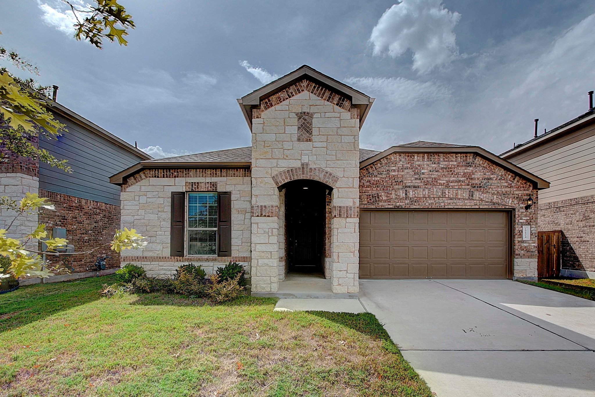 French country inspired facade with stone siding, a front yard, concrete driveway, an attached garage, and brick siding