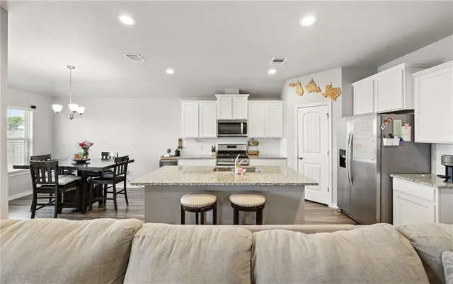 a kitchen with stainless steel appliances granite countertop a refrigerator a stove top oven a sink a dining table and chairs with wooden floor