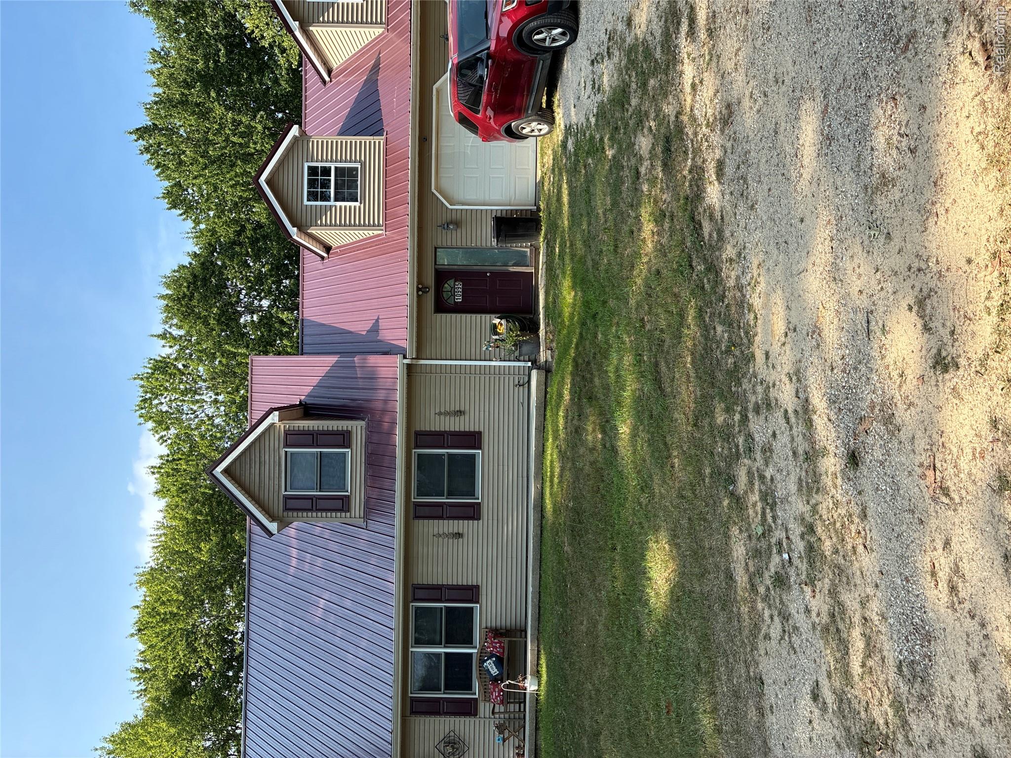 10995 East Isabella County Line Road Coleman, MI 48618 - Photo 11 of 76 Beige horizontal siding with red metal roofing, dormer windows, and an attached garage