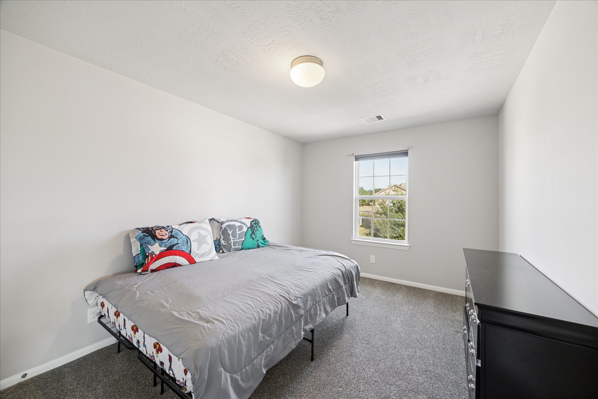 7610 Retama Terrace Lane Humble, TX 77338 - Photo 11 of 14 This photo showcases a cozy bedroom with neutral walls, a large window providing natural light, and a simple ceiling light. The room features a bed with themed bedding and a dresser, offering a comfortable and inviting space.