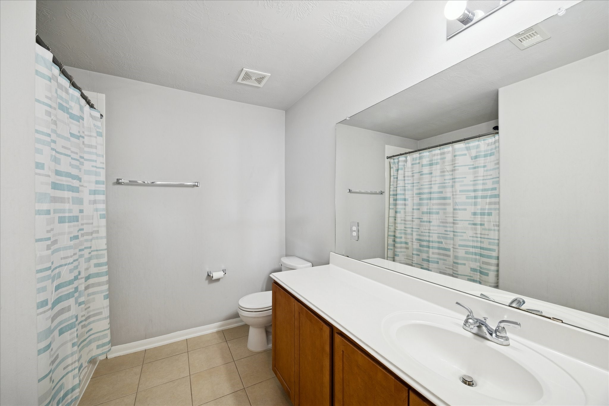 7610 Retama Terrace Lane Humble, TX 77338 - Photo 12 of 14 This bathroom features a clean, modern design with a large mirror, single-sink vanity, and a bathtub with a patterned shower curtain. Neutral walls and tiled flooring add to the bright, spacious feel.