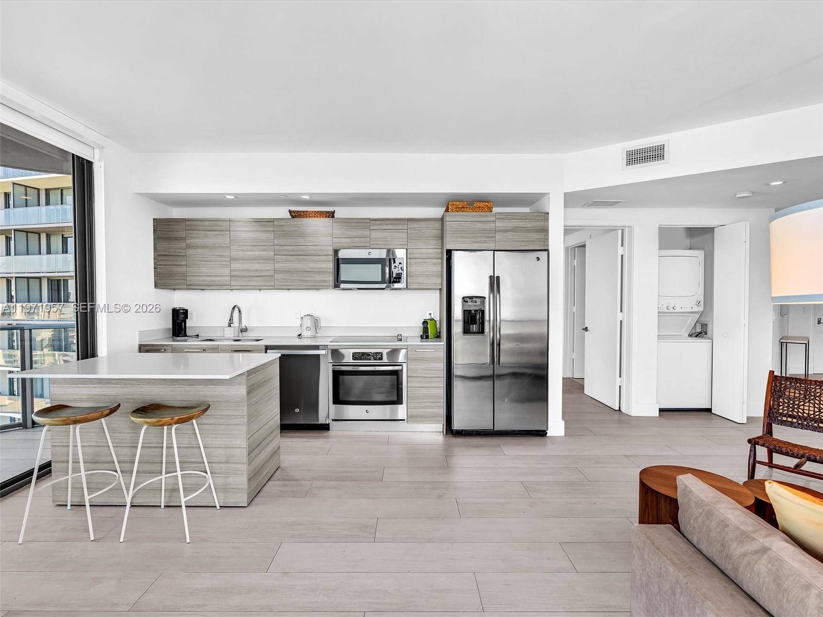 121 Northeast 34th Street, Unit 2016 Miami, FL 33137 - Photo 48 of 55 a large white kitchen with stainless steel appliances kitchen island granite countertop a refrigerator and a stove top oven