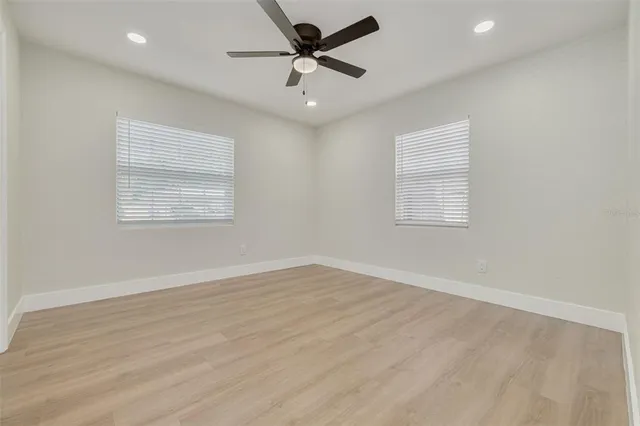 an empty room with wooden floor ceiling fan and windows