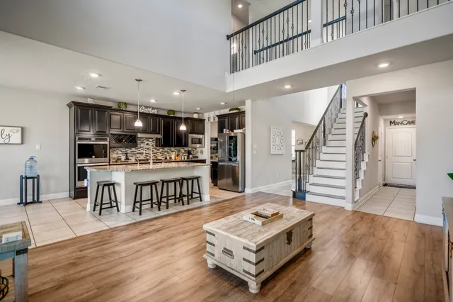 a living room with stainless steel appliances kitchen island granite countertop a refrigerator a stove a sink dishwasher and a dining table with wooden floor
