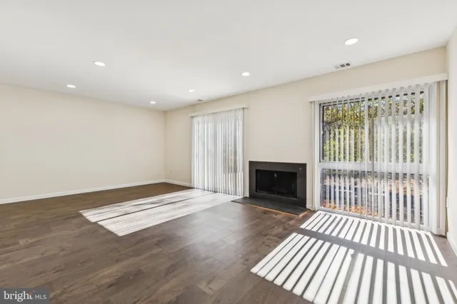 a view of an empty room with wooden floor fireplace and a window