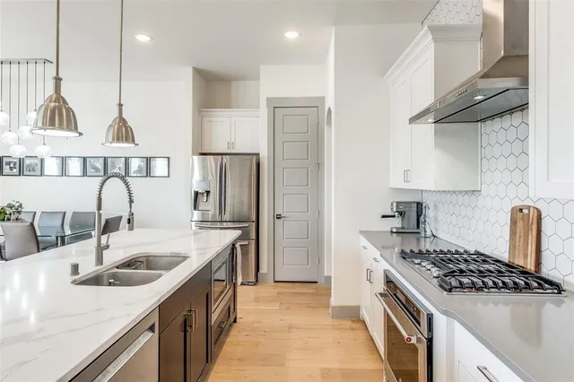 a kitchen with stainless steel appliances granite countertop a stove a sink dishwasher a refrigerator and a dining table with wooden floor