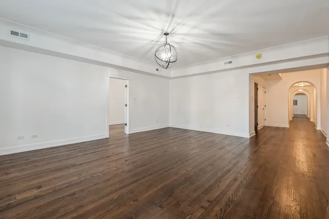 a view of an empty room with wooden floor and fan