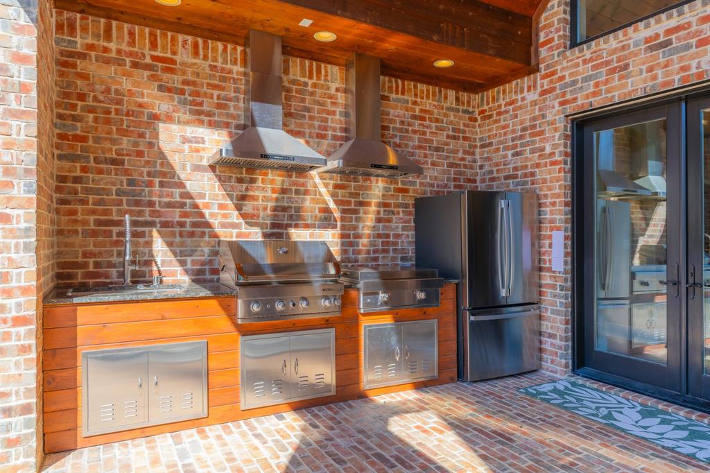 594 Turner Warnell Road Mansfield, TX 76063 - Photo 33 of 38 Outdoor kitchen featuring gas grill and griddle, wall chimney exhaust hood, brick flooring, brick wall, freestanding refrigerator, and a wood ceiling with exposed beams