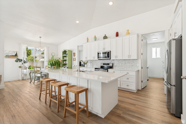 683 Kings Landing Tooele, UT 84074 - Photo 5 of 39 Bright kitchen featuring a substantial island with countertop seating, white shaker cabinetry, stainless steel appliances, and a geometric tile backsplash