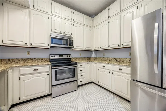a kitchen with stainless steel appliances granite countertop white cabinets and a refrigerator