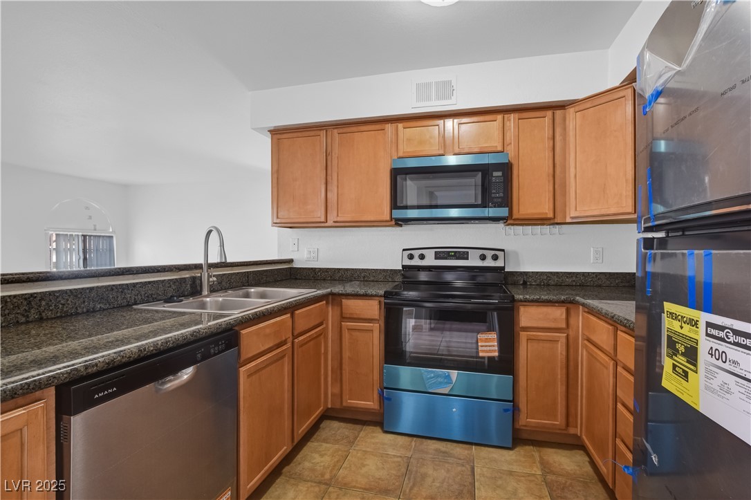 9325 West Desert Inn Road, Unit 177 Las Vegas, NV 89117 - Photo 5 of 13 Kitchen featuring stainless steel appliances, brown cabinetry, and light tile patterned floors