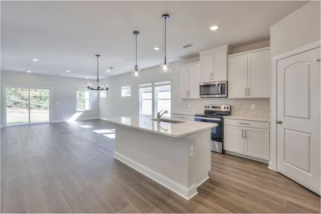 a kitchen with kitchen island granite countertop a stove a sink a refrigerator and white cabinets with wooden floor