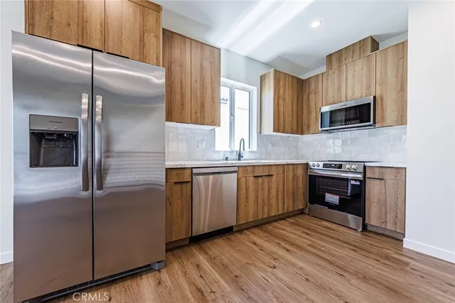 a kitchen with stainless steel appliances granite countertop a refrigerator a stove and a sink with wooden floor