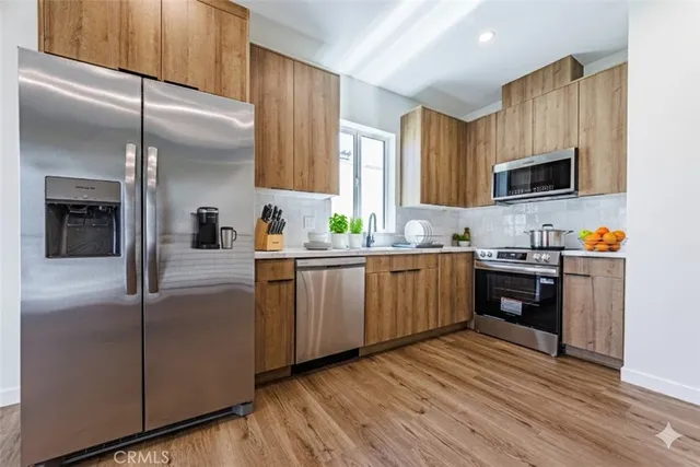 a kitchen with stainless steel appliances granite countertop a refrigerator a sink dishwasher a oven with wooden cabinets and floor