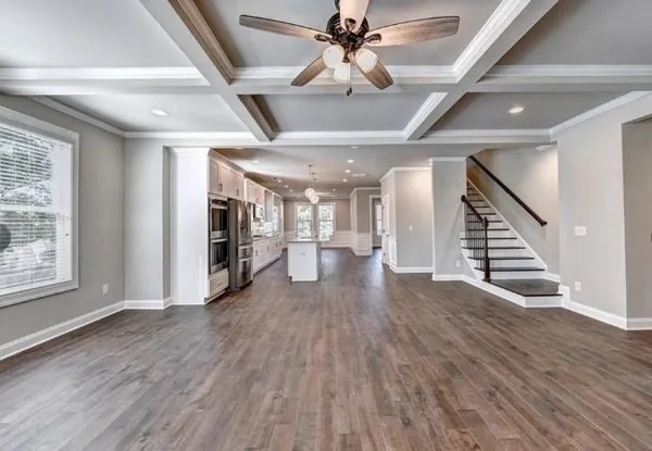 an empty room with wooden floor staircase and windows