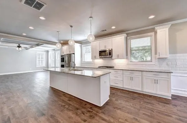 a kitchen with stainless steel appliances granite countertop a sink a stove a refrigerator and white cabinets with wooden floor