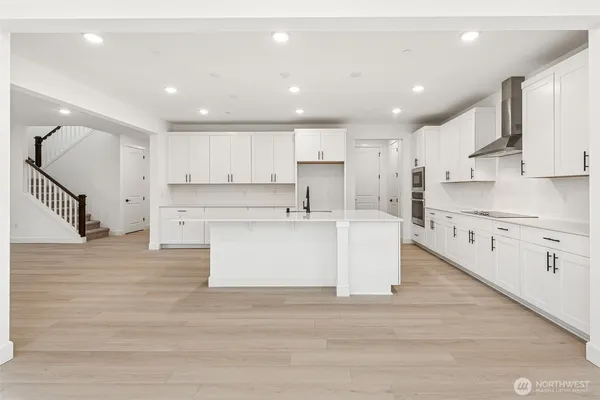 a large kitchen with stainless steel appliances kitchen island a stove a sink dishwasher a refrigerator and white cabinets with wooden floor