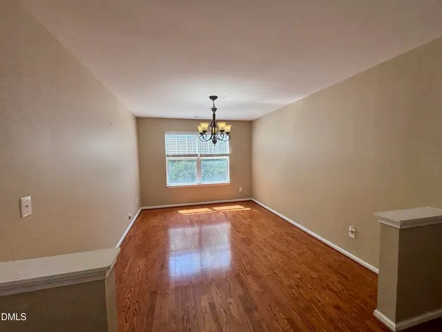 an empty room with wooden floor chandelier and windows