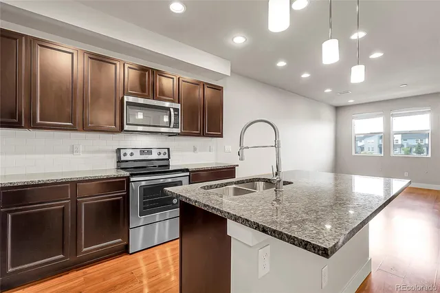 a kitchen with stainless steel appliances granite countertop a refrigerator a stove and a sink with wooden floor