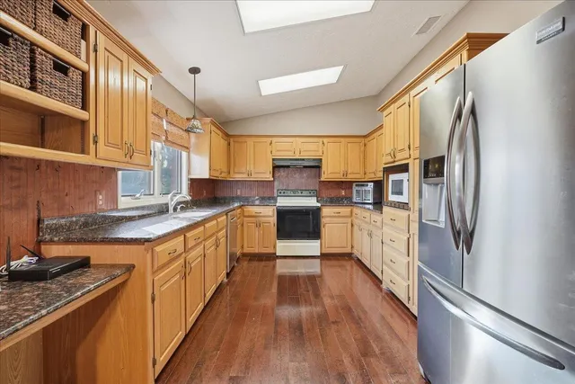 a kitchen with stainless steel appliances granite countertop a refrigerator a sink dishwasher a stove and a wooden floor