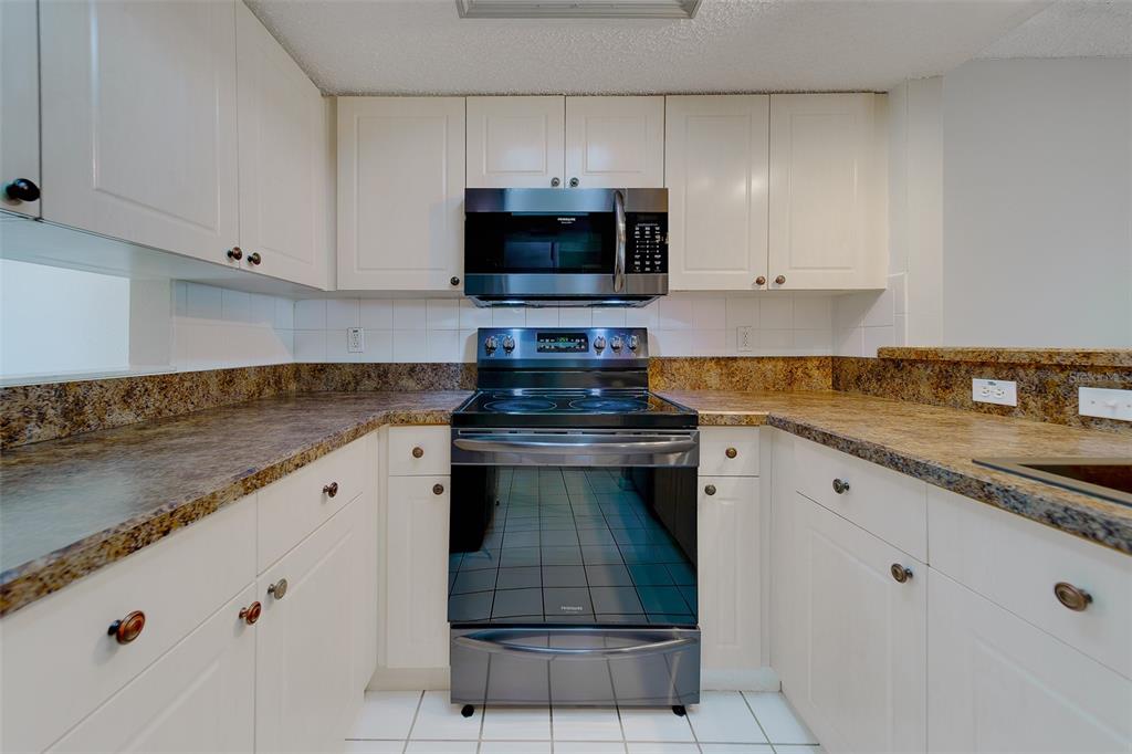 9241 Jake's Path Largo, FL 33771 - Photo 31 of 46 a kitchen with granite countertop a stove a sink and a white cabinets