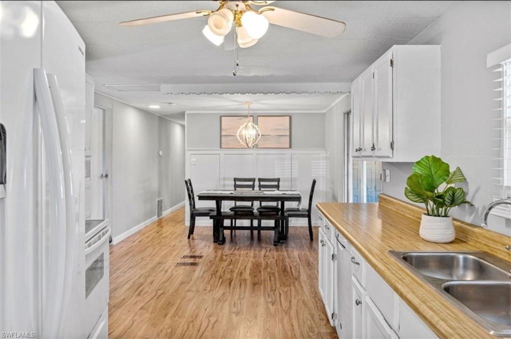 407 Cape Florida Way Naples, FL 34104 - Photo 11 of 27 Kitchen featuring white appliances, white cabinets, light countertops, decorative light fixtures, and light wood finished floors