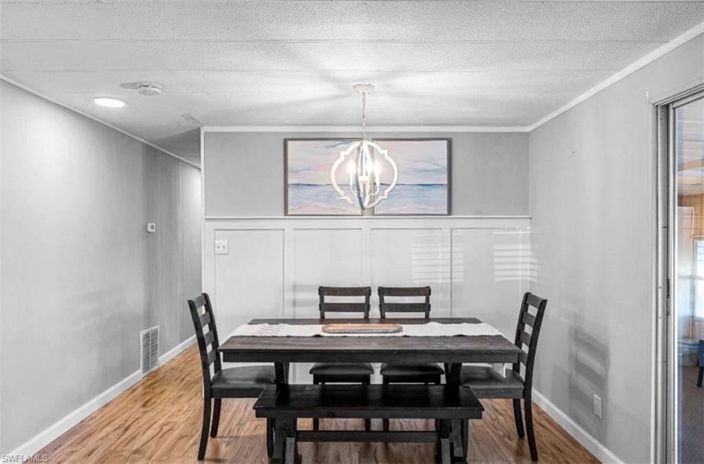 407 Cape Florida Way Naples, FL 34104 - Photo 4 of 27 Dining space with a chandelier, wood finished floors, crown molding, a decorative wall, and a textured ceiling