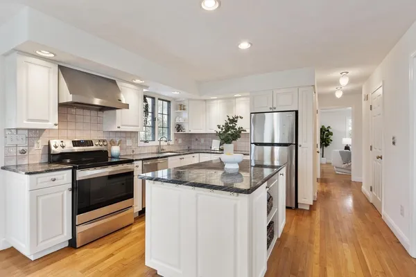 a kitchen with stainless steel appliances granite countertop a refrigerator a stove a sink dishwasher and white cabinets with wooden floor