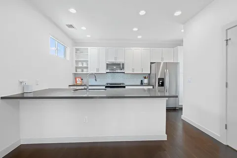 a large kitchen with stainless steel appliances a sink a stove a microwave a refrigerator and white cabinets with wooden floor