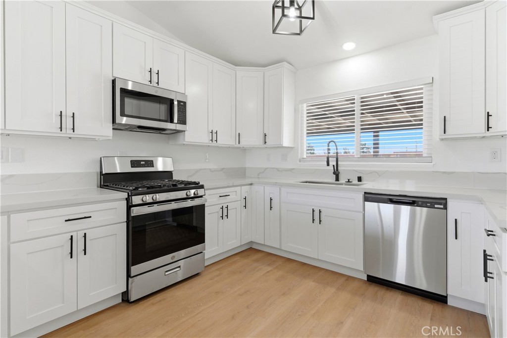 22557 Ojai Road Apple Valley, CA 92308 - Photo 11 of 57 a kitchen with stainless steel appliances white cabinets a sink a stove a microwave and wooden floors