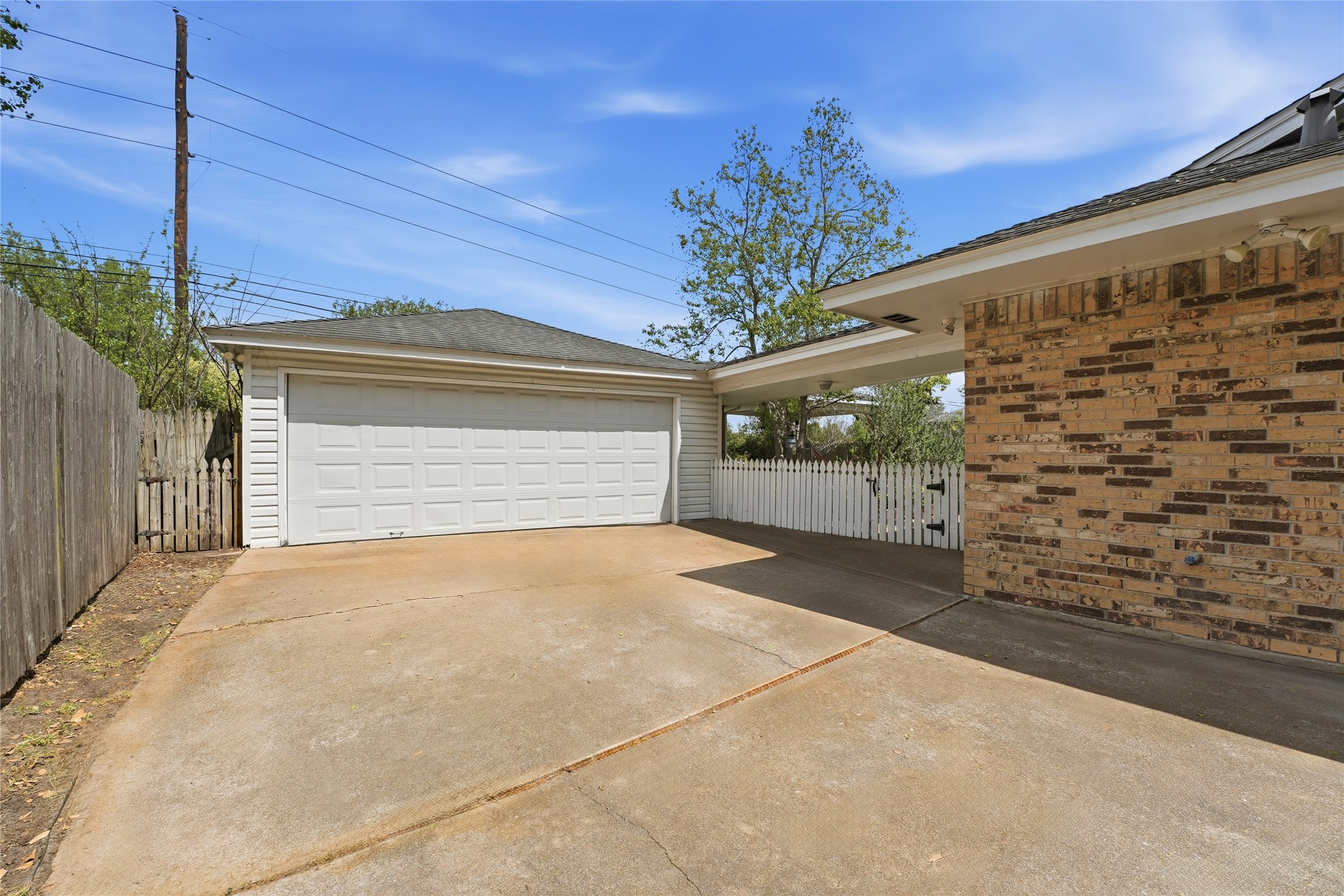 22338 Wetherburn Lane Katy, TX 77449 - Photo 23 of 36 Spacious driveway with a detached two-car garage, featuring a brick exterior and a white picket fence for added privacy to the backyard.