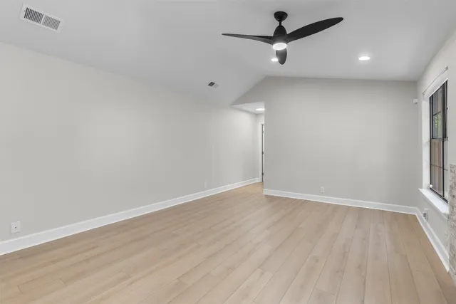 an empty room with wooden floor ceiling fan and window
