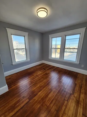 a view of an empty room with wooden floor and window