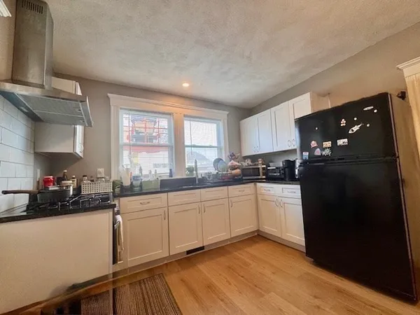 a kitchen with a sink dishwasher a refrigerator and white cabinets with wooden floor