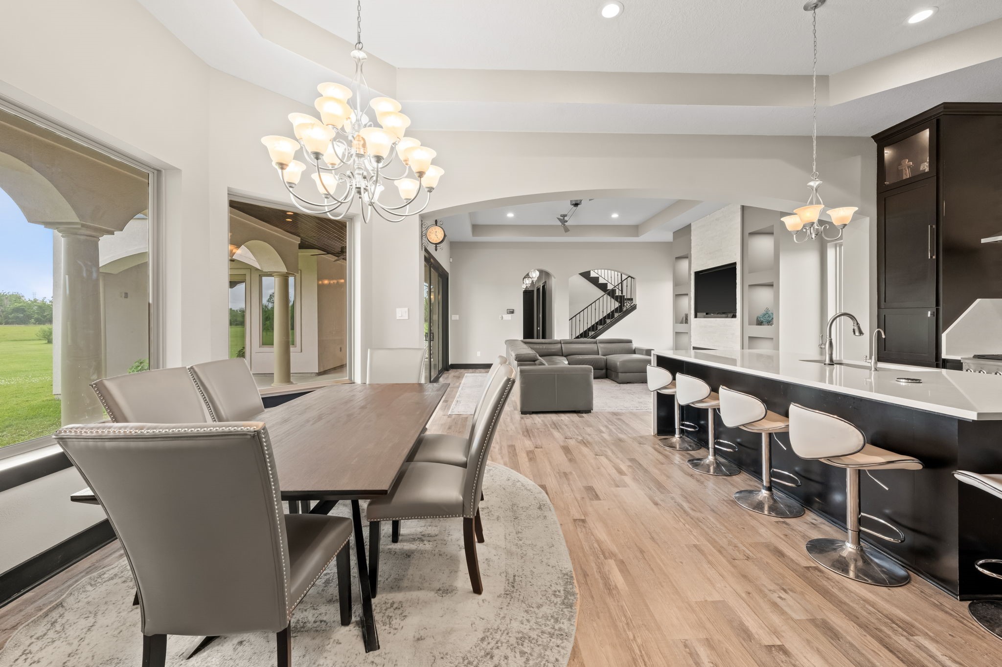 2856 Wolcek Road Crosby, TX 77532 - Photo 11 of 48 spacious, open-concept living area with modern design elements. It features a large dining table under an elegant chandelier, a sleek kitchen with a large island and bar seating, and a cozy living room with a view of the staircase. Expansive windows offer plenty of natural light and views of green outdoor space.