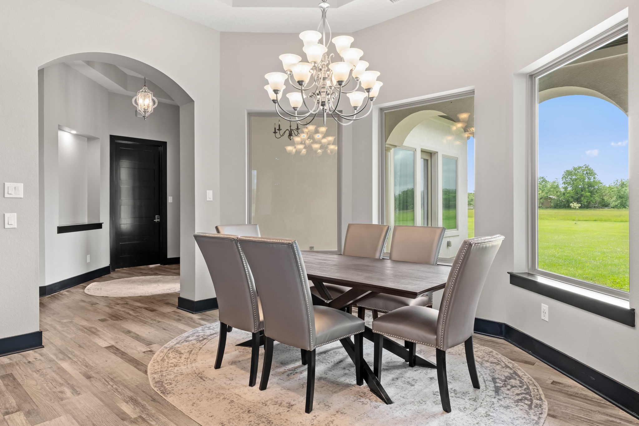 2856 Wolcek Road Crosby, TX 77532 - Photo 16 of 48 a bright, modern dining room with large windows offering scenic views of a green lawn. The space is enhanced by archways and soft neutral tones, creating a welcoming ambiance.