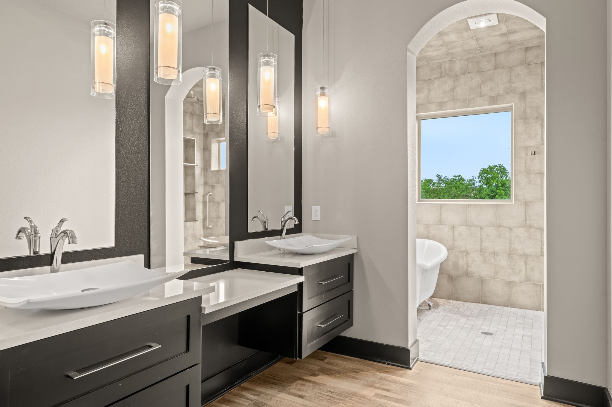 2856 Wolcek Road Crosby, TX 77532 - Photo 20 of 48 This modern bathroom features a sleek double vanity with vessel sinks, elegant pendant lighting, and an arched entry leading to a spacious shower area (wet room) with a large window offering natural light and scenic views.
